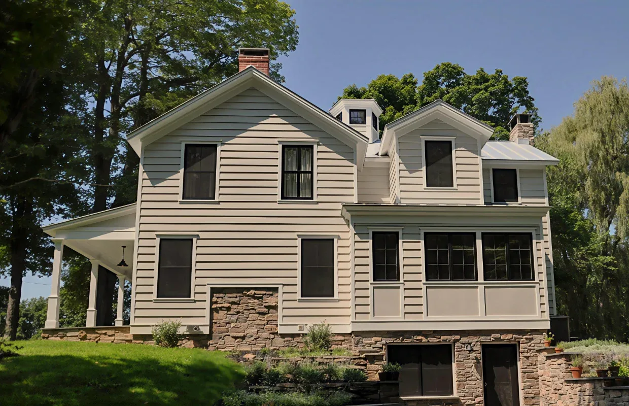 Two-story house exterior with wood siding and stone foundation featuring multiple windows and a covered porch.