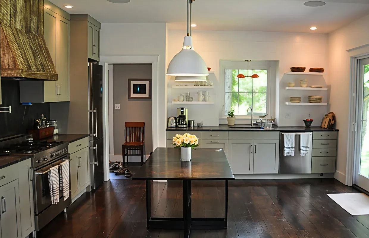 Modern kitchen features light gray cabinetry, black countertops, stainless steel appliances, and open shelving around a window above the sink.