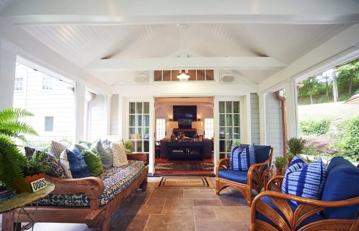 Covered patio area with wooden sofa and wicker chairs, tiled floor, and view into living room at Frog Pond Farm project.