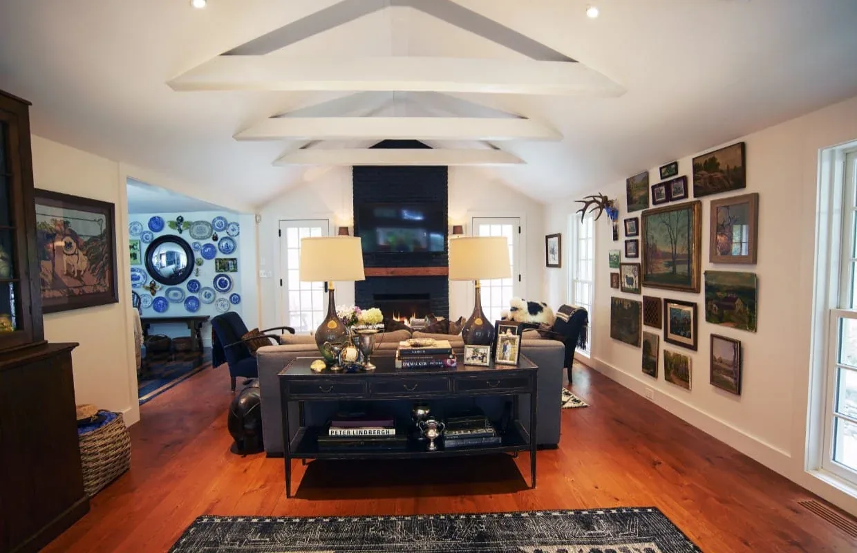 This living room features a vaulted ceiling with exposed beams, a black fireplace, and hardwood flooring with gallery wall art.