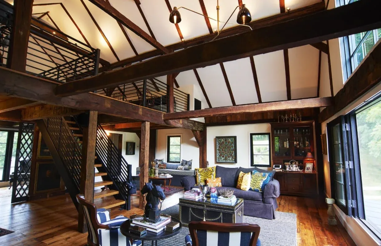 Living room with vaulted ceiling, exposed wood beams, and metal staircase in a rustic style home.