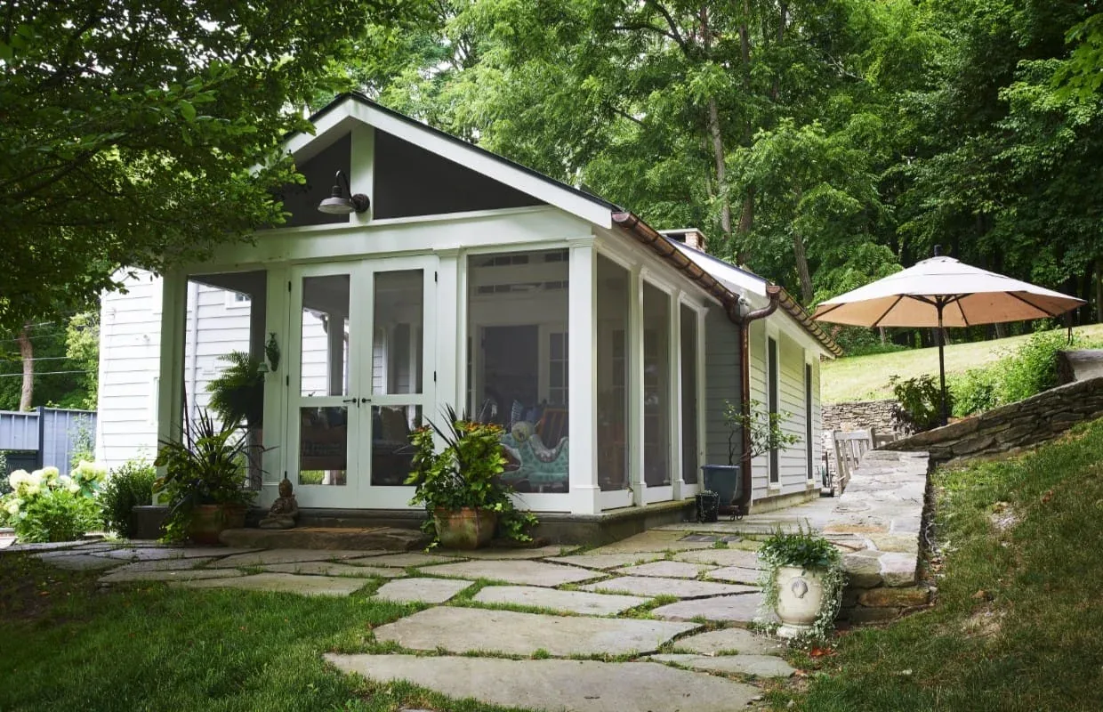 The FROG POND FARM pool house features white siding, screened porch, and stone patio with nearby umbrella seating.