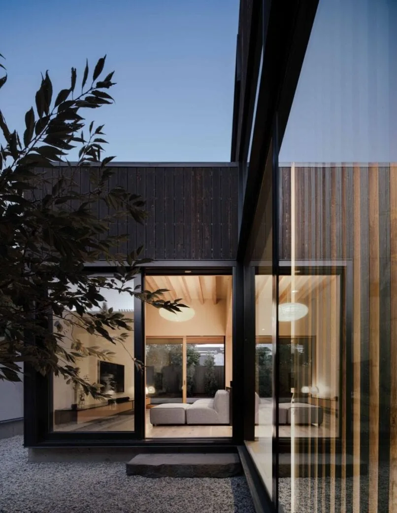 Cupertino Courtyard House features dark vertical wood siding and floor-to-ceiling glazing around a gravel courtyard.