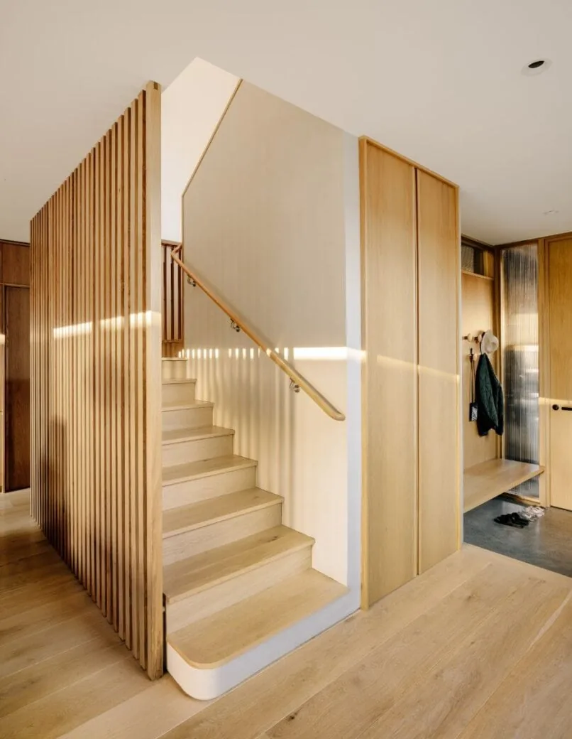 Staircase with vertical wood slat divider and light wood flooring in the Cupertino Courtyard House.