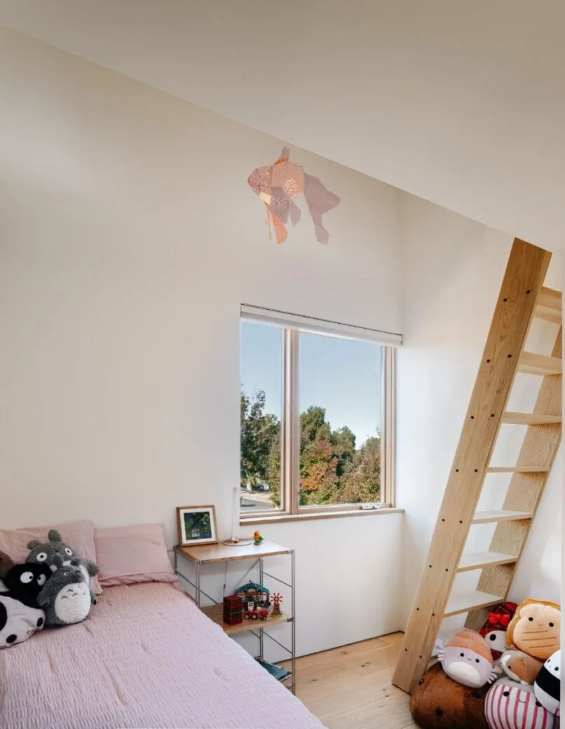 Bedroom with light wood floors, a simple metal shelf, and a ladder beside a large window showing outdoor greenery.