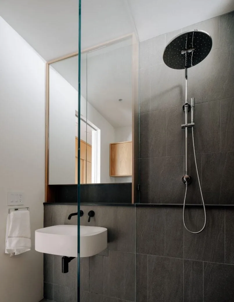 Bathroom features a wall-mounted rain showerhead, matte black fixtures, and a minimal sink with a large mirror reflecting interior cabinetry.