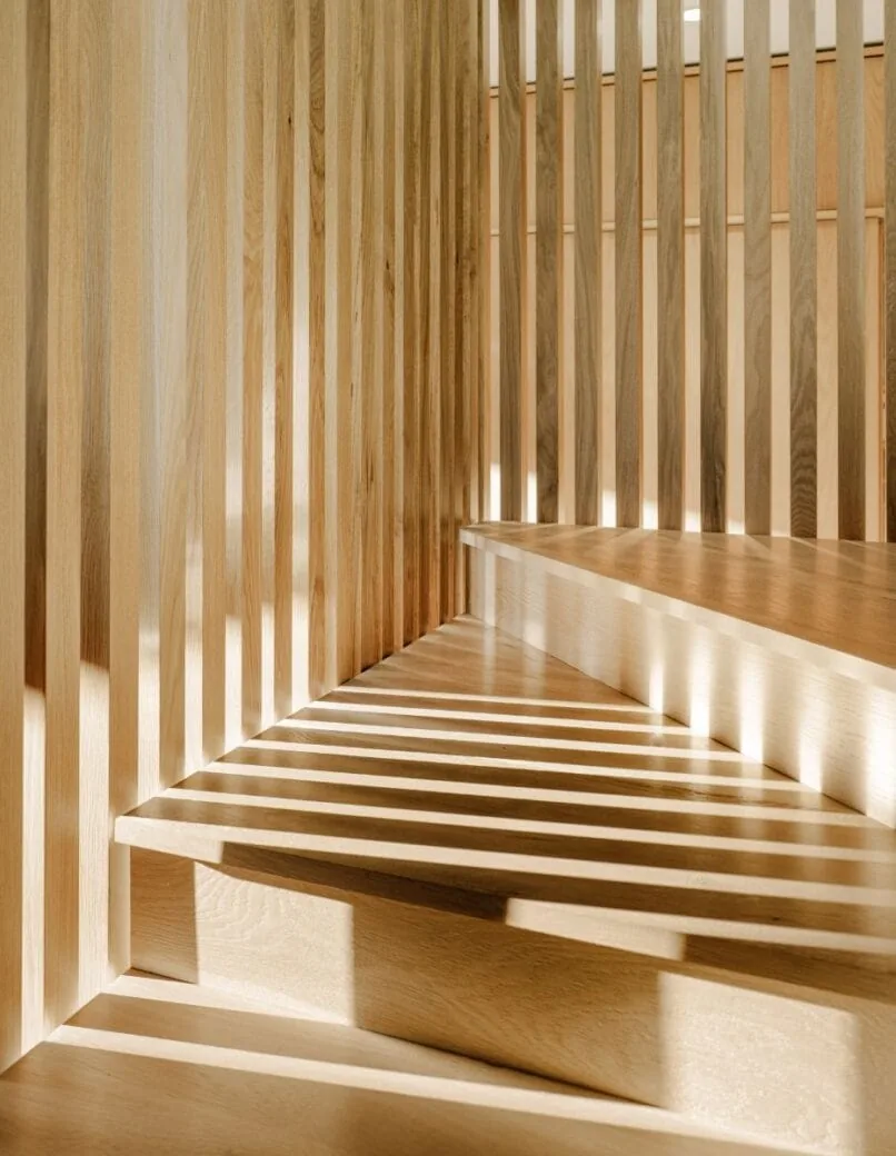Light wood steps with vertical wood slat walls creating linear striped shadows from sunlight.