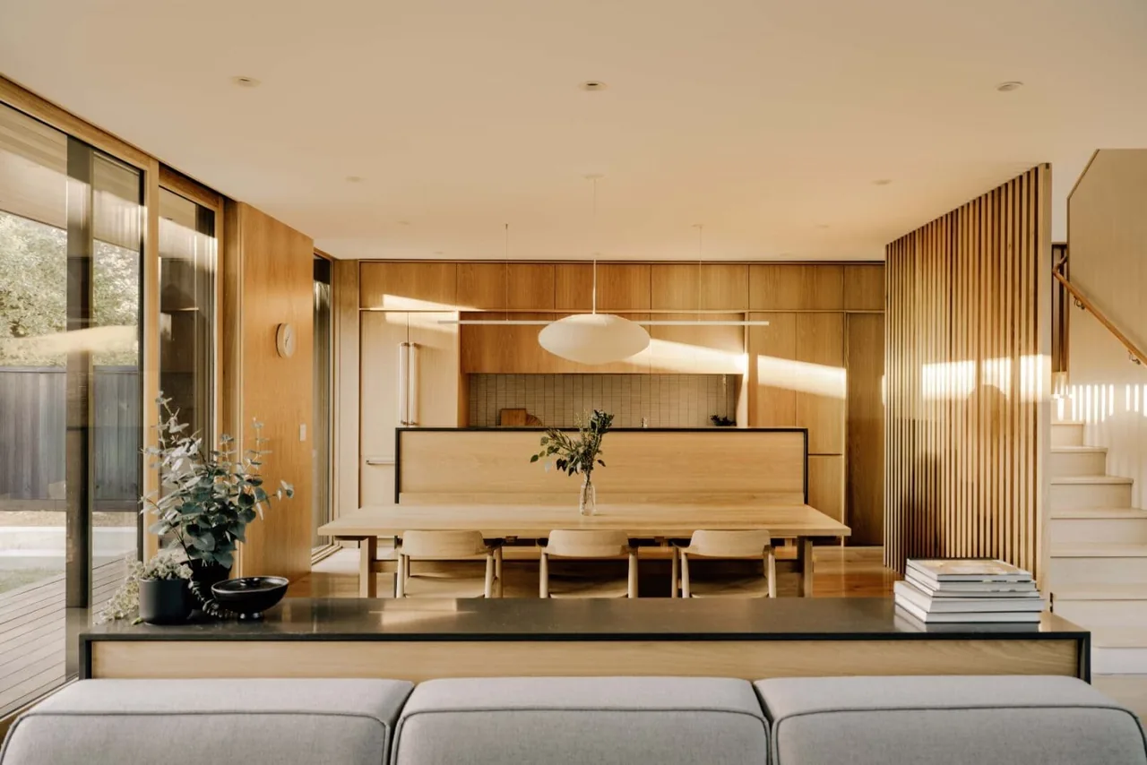 The Cupertino Courtyard House features a wood-paneled interior with a dining table, built-in bench, and modern pendant lighting.