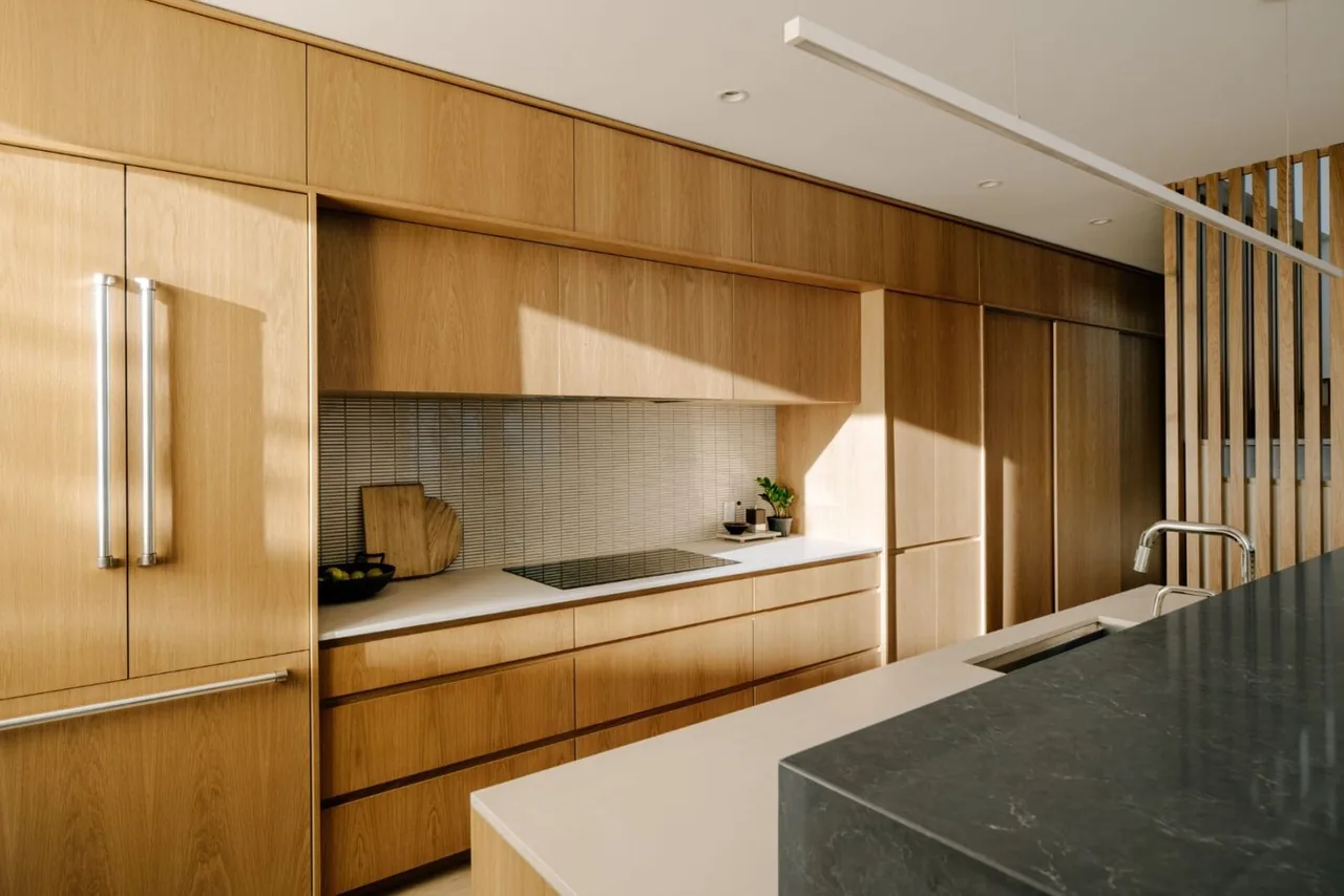 Kitchen in Cupertino Courtyard House features light wood cabinets with white countertops and a black marble island with sink and faucet.