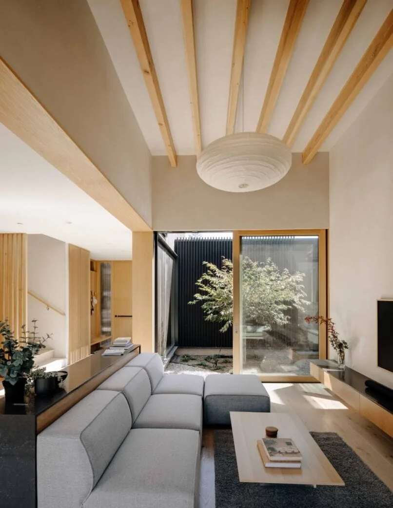 Living room with light wood ceiling beams, gray sectional, and large sliding glass door to courtyard in Cupertino Courtyard House by SHED Architecture.