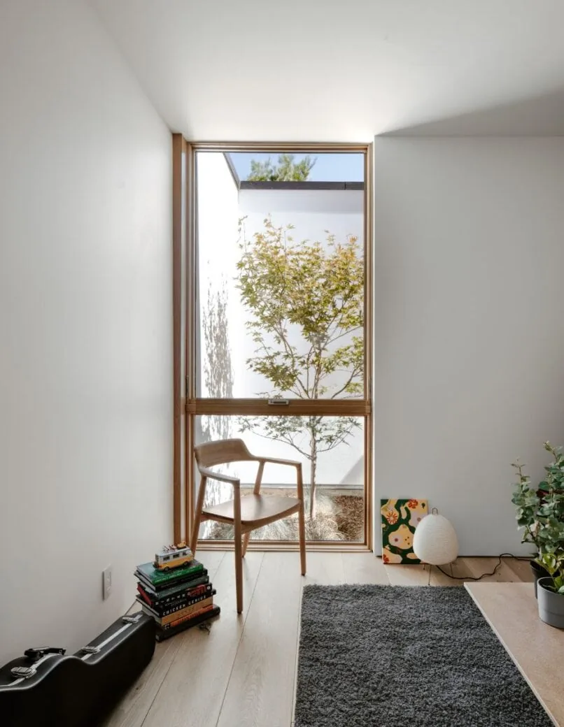 Light-filled room with floor-to-ceiling wooden framed window overlooking a small courtyard tree.