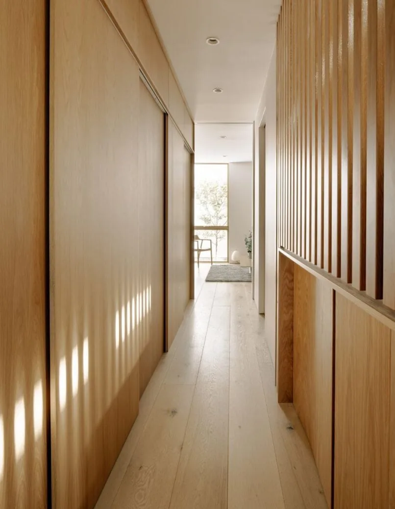Hallway features light wood flooring and vertical wood slats creating striped light patterns.