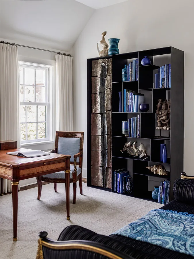This office in Shelter Island House features classic wooden furniture and a large black shelf with various art pieces and blue accents.