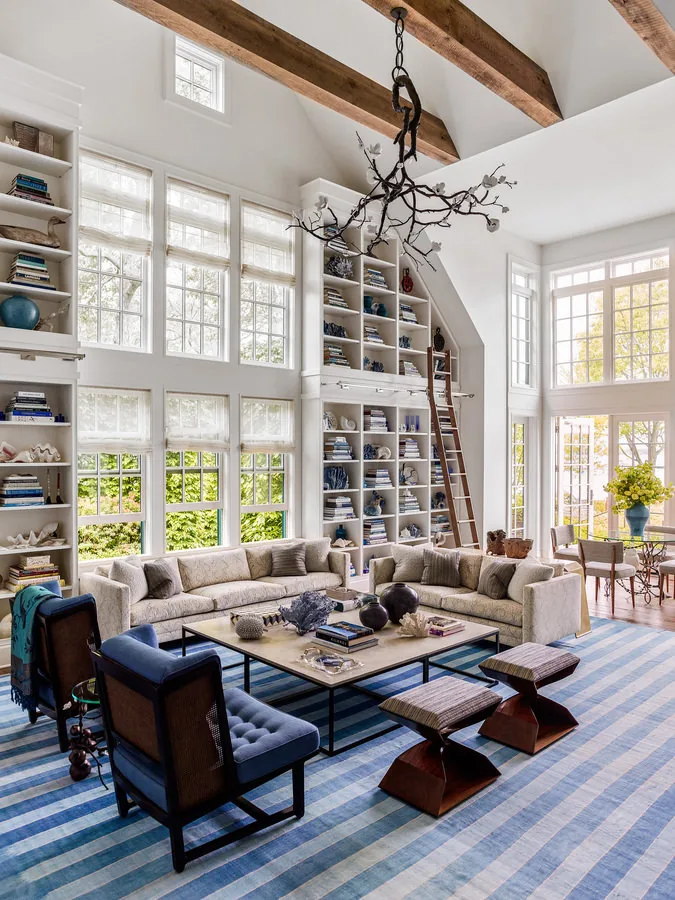 Living room featuring vaulted ceiling with wooden beams, built-in shelving, and large windows with shades.