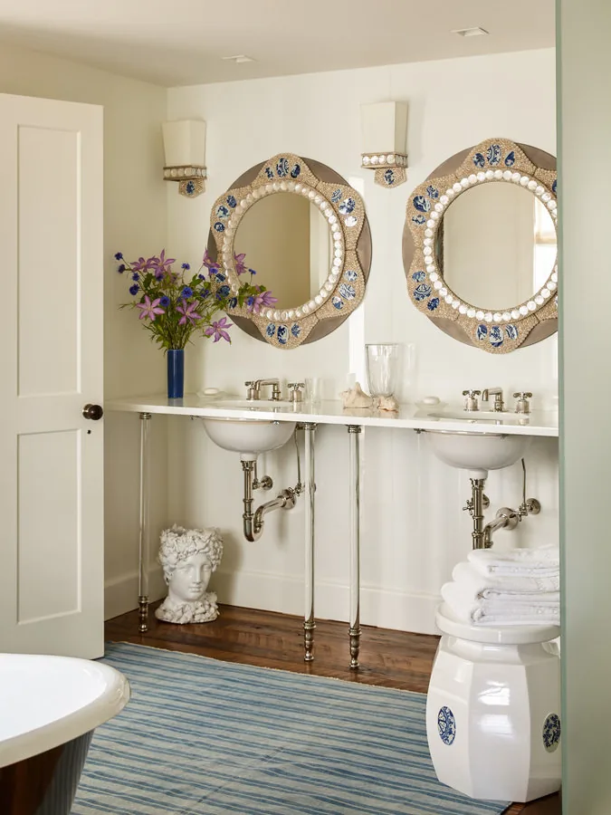 Bathroom features double pedestal sinks with metal piping, ornate round mirrors, and unique decor accents.