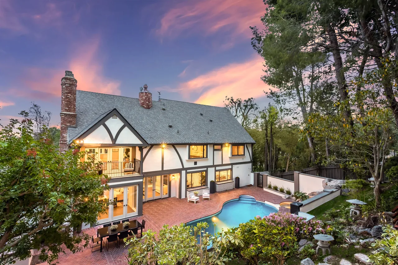 Back exterior view of a two-story traditional home with pool and patio at sunset.