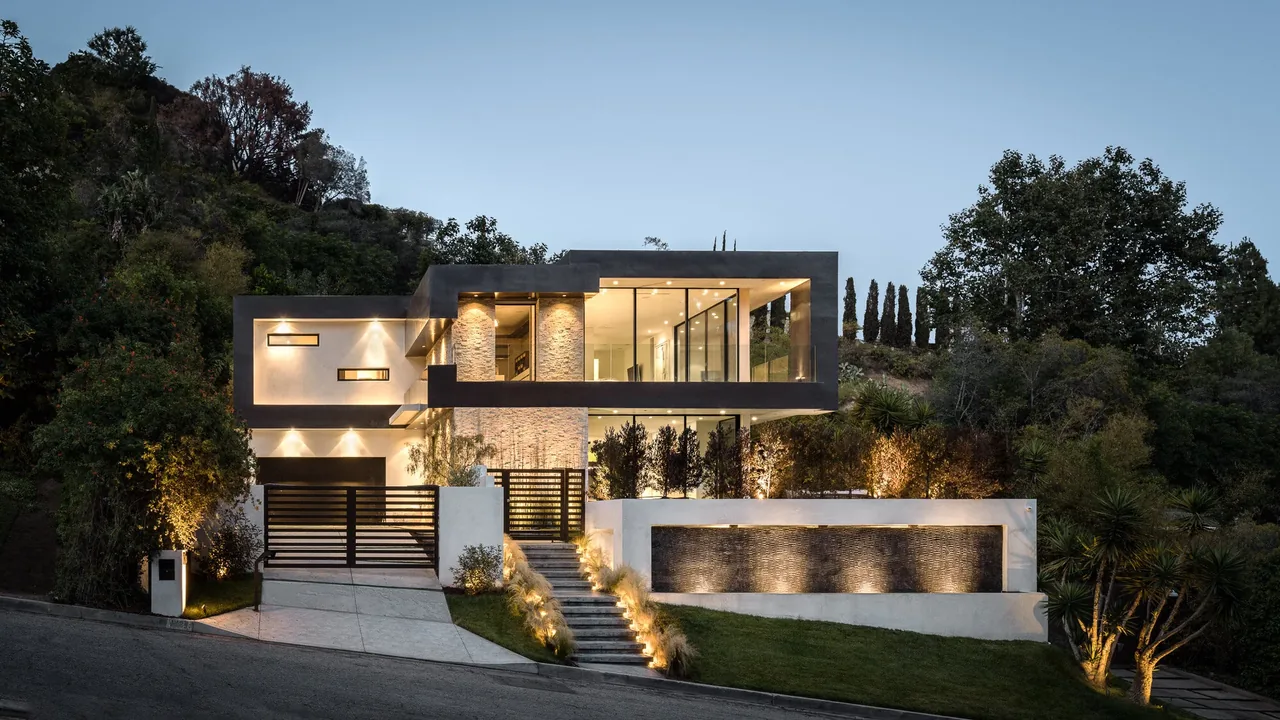 The Rising Glen project features a modern two-story home with prominent glass walls and exterior stone accents.