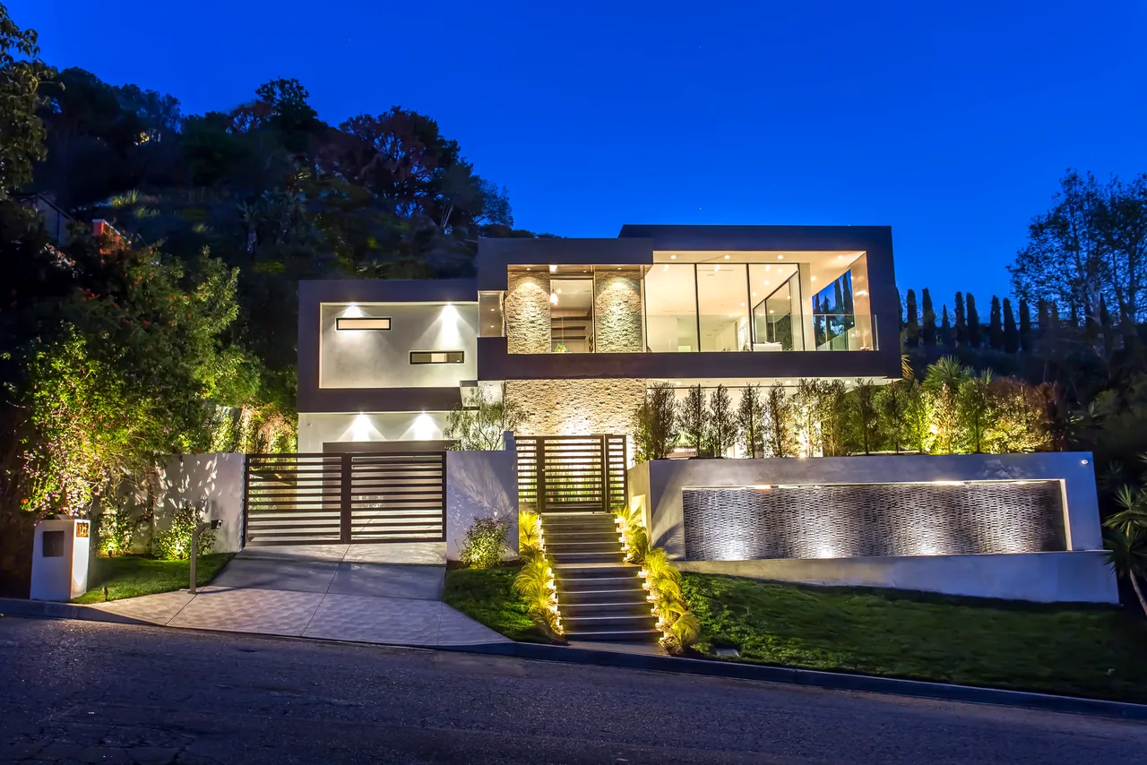 Modern flat-roof house with illuminated stone wall and large glass windows at night in Los Angeles.