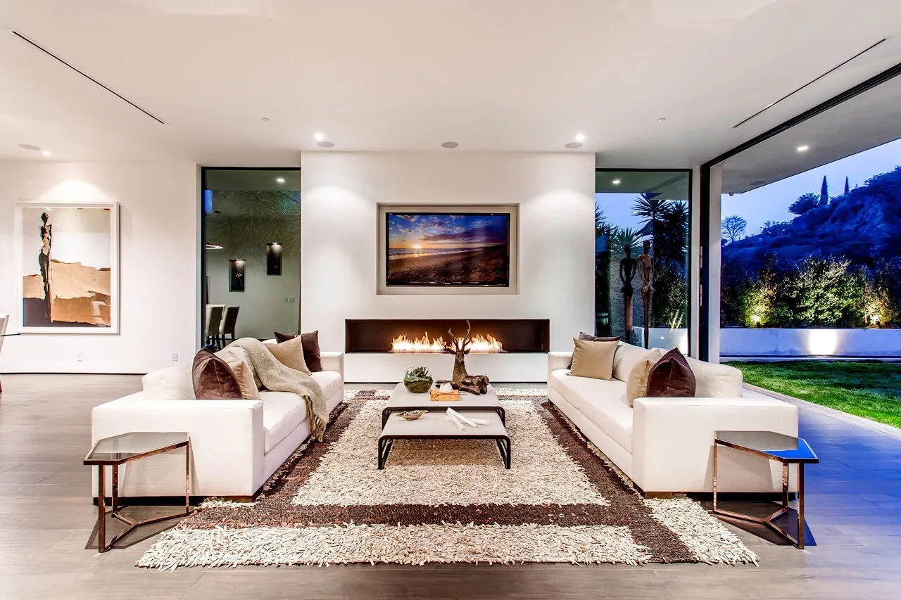 Living room features minimalist white sofas, a linear fireplace, and large sliding glass doors opening to an outdoor space.