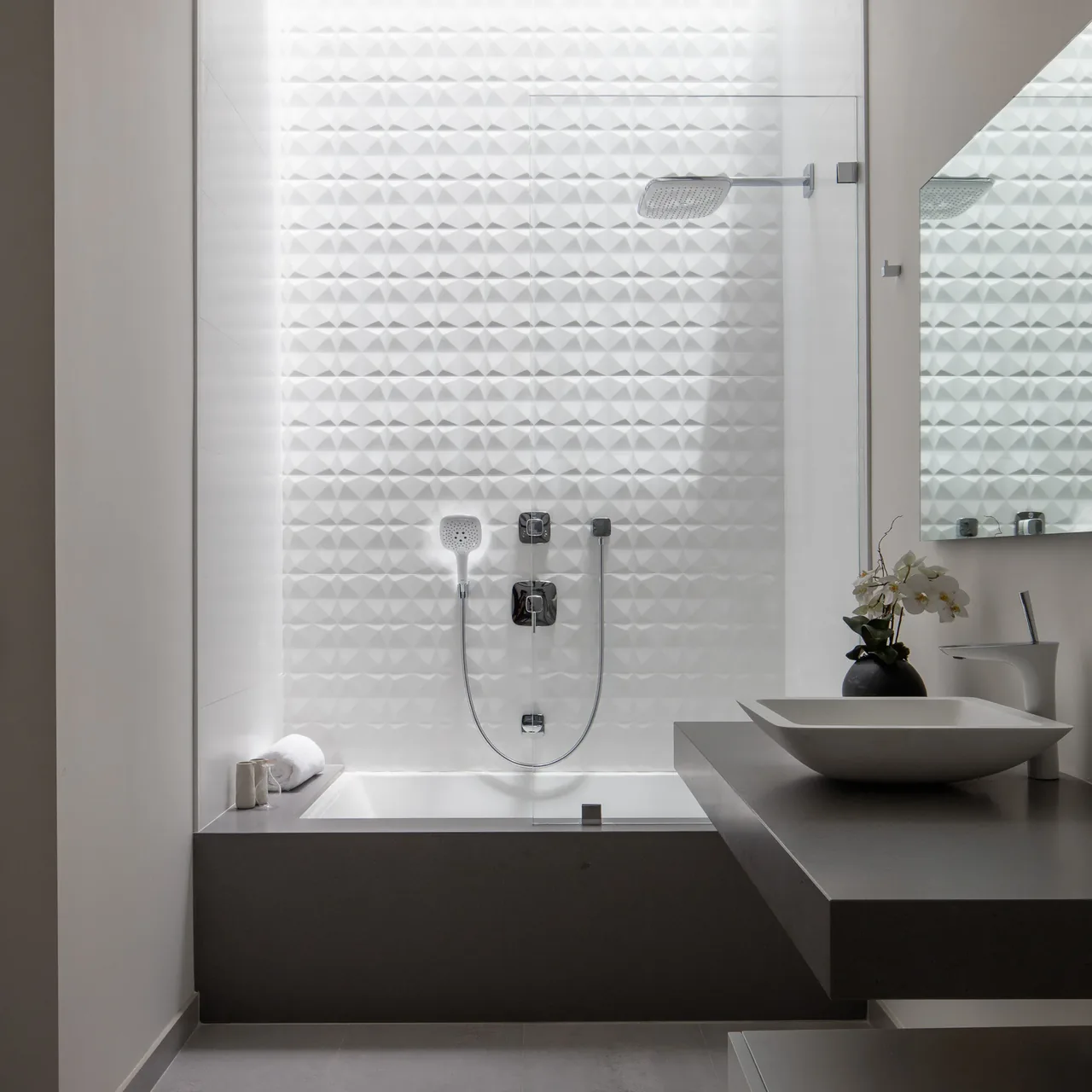 Minimalist bathroom with textured white tiles, bathtub, and a wall-mounted shower head.