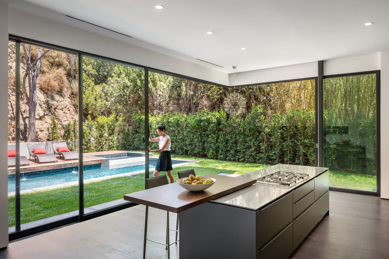 Kitchen featuring large corner glazing and sliding glass door opening to a poolside backyard.