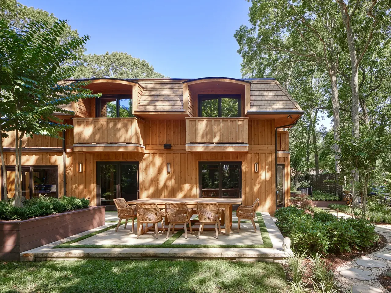 The Tidewater project features a wood-sided home with curved dormer roofs and an outdoor dining patio in a landscaped backyard.