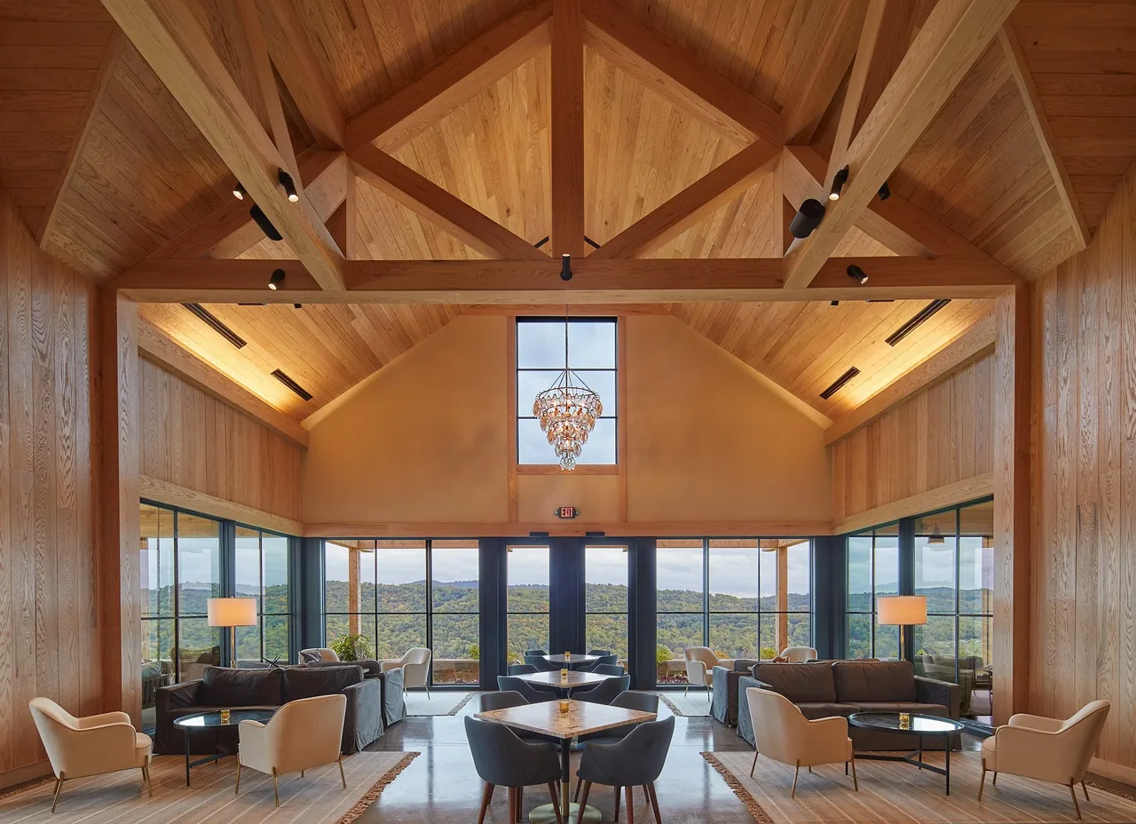Lounge area inside Crimson Lane Vineyard features exposed timber framing, floor-to-ceiling windows, and a chandelier.