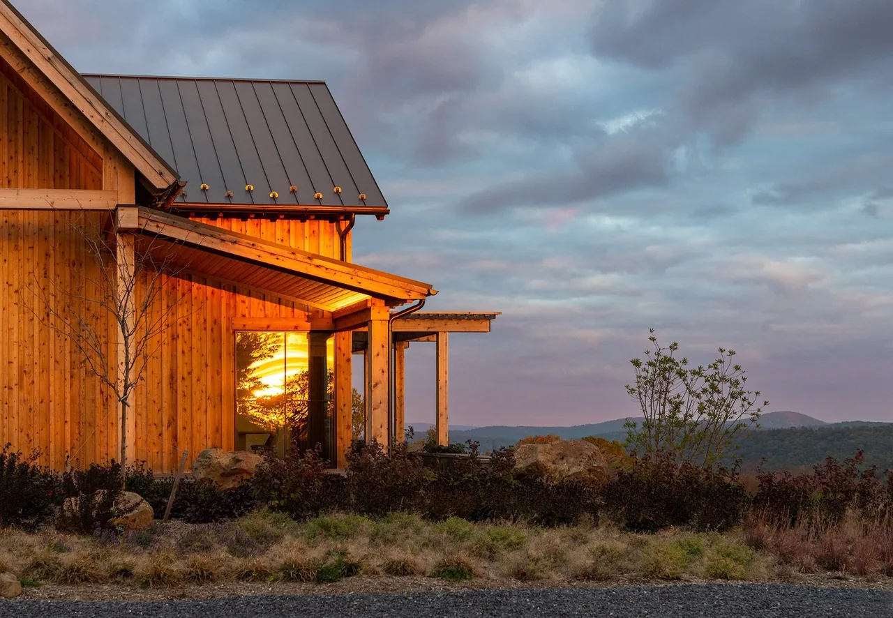 Crimson Lane Vineyard features a timber-framed exterior with standing seam metal roof and natural wood siding, illuminated by sunset reflections.
