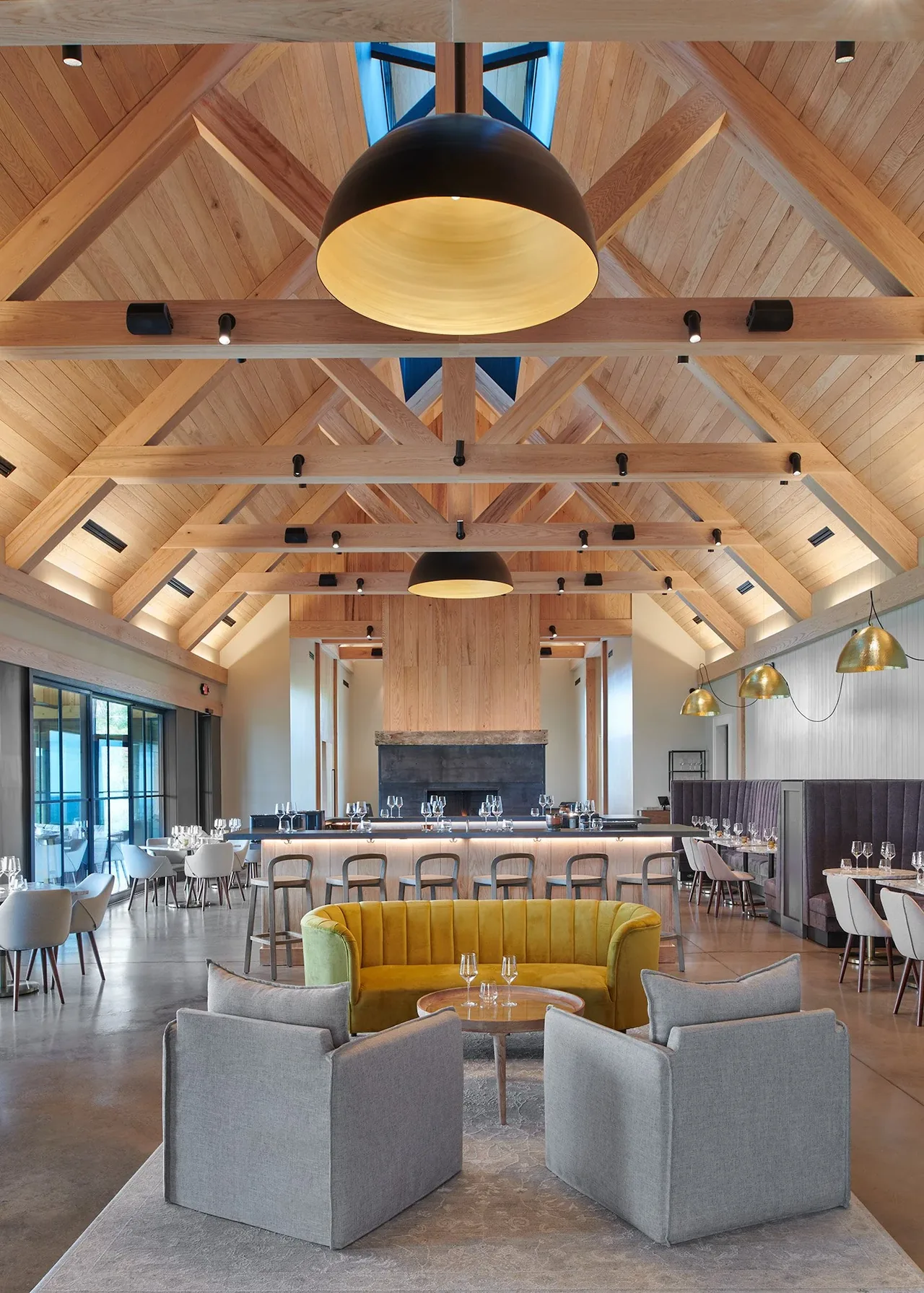 Interior shows a vaulted ceiling with timber framing, a central fireplace, and seating areas including a curved yellow sofa.