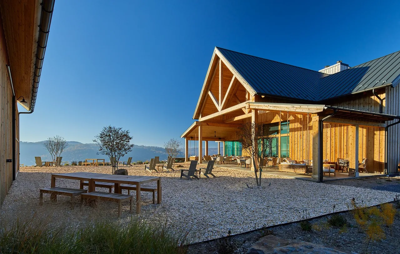 Timber-framed building with triangular gable roof and outdoor seating on gravel at Crimson Lane Vineyard during sunset.