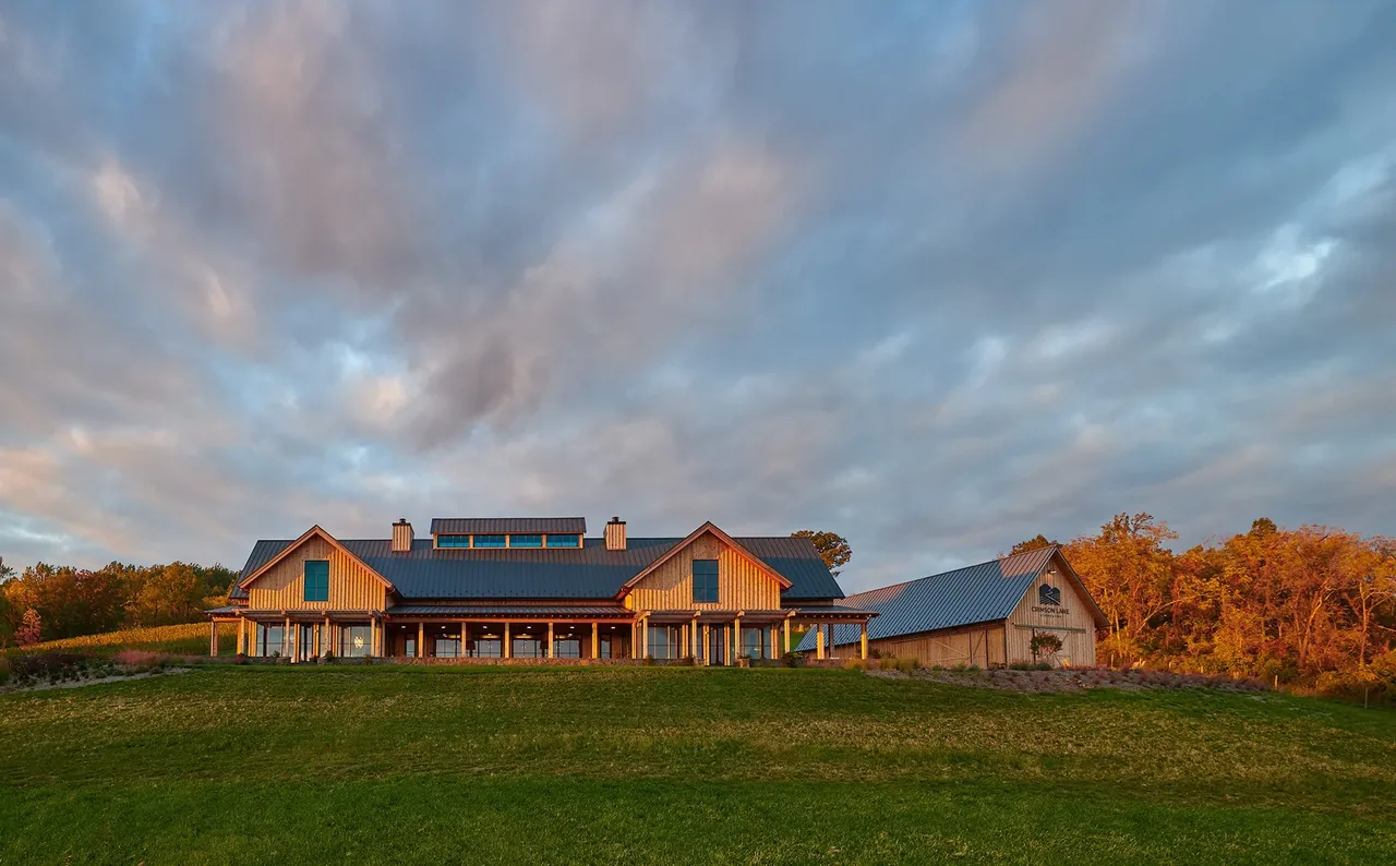 Crimson Lane Vineyard building with timber framing and metal roof on a grassy hillside at sunset.