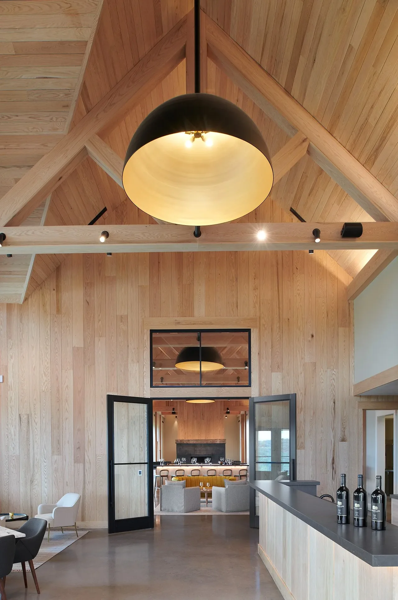 Vaulted ceiling interior with timber framing, wood panel walls, and a large black pendant light in Crimson Lane Vineyard project.