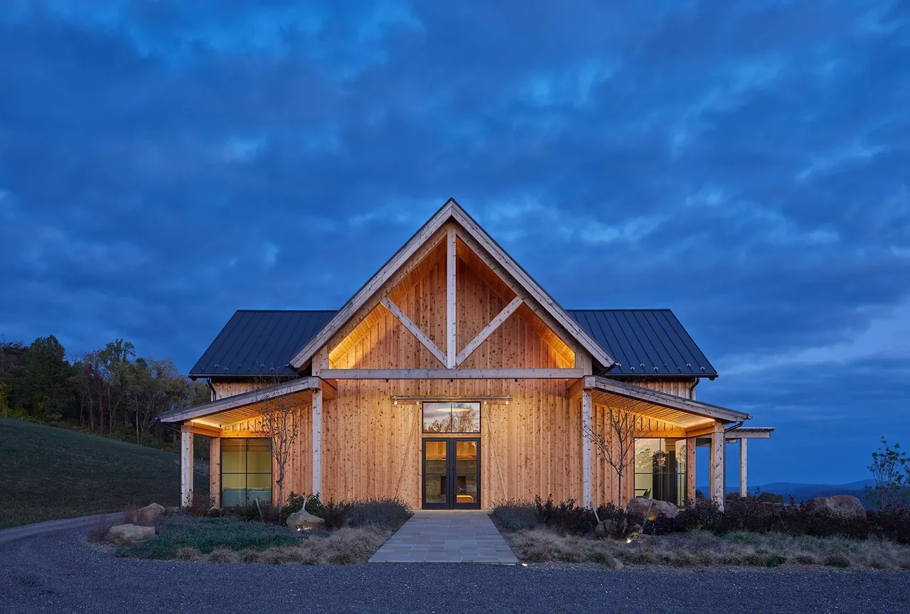 Front exterior view of a wood barn-style building with a triangular gable roof at dusk.