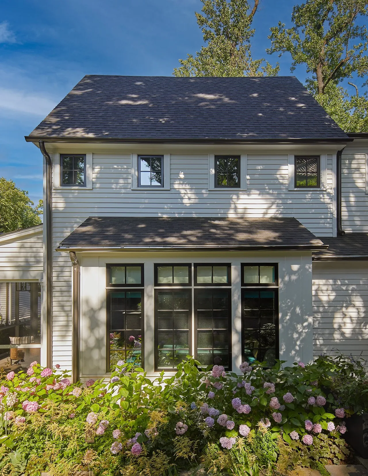 Cathedral View project by Moore Architects features multi-pane black-trim windows and a landscaped garden with blooming hydrangeas.
