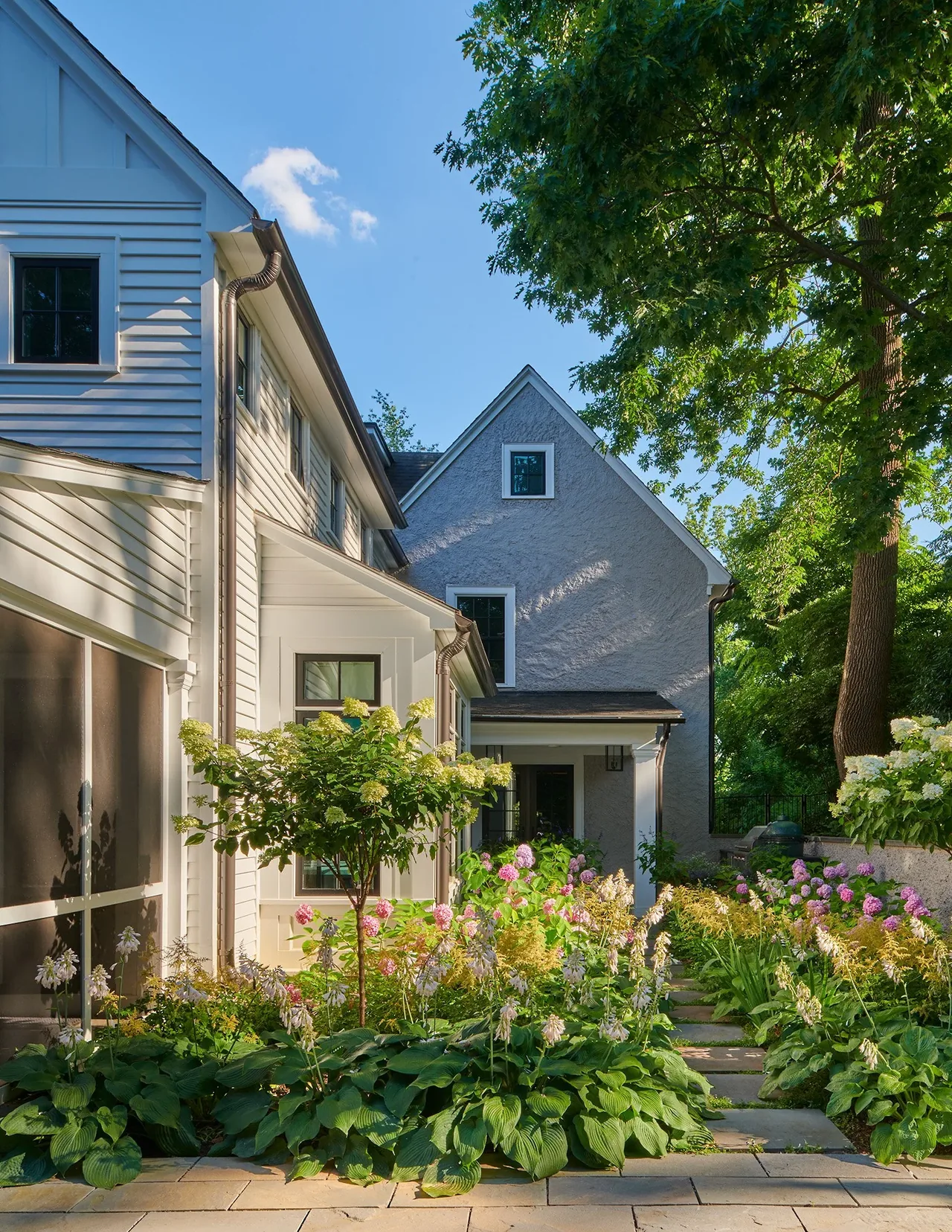 The home features a combination of white horizontal siding and textured gray stucco, with landscaped garden and stone pathway leading to a sheltered entrance.