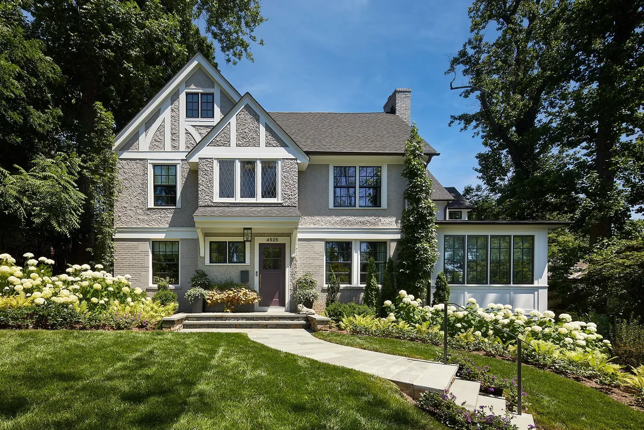 Tudor-style home with textured stucco facade and multi-pane windows surrounded by lush landscaping.