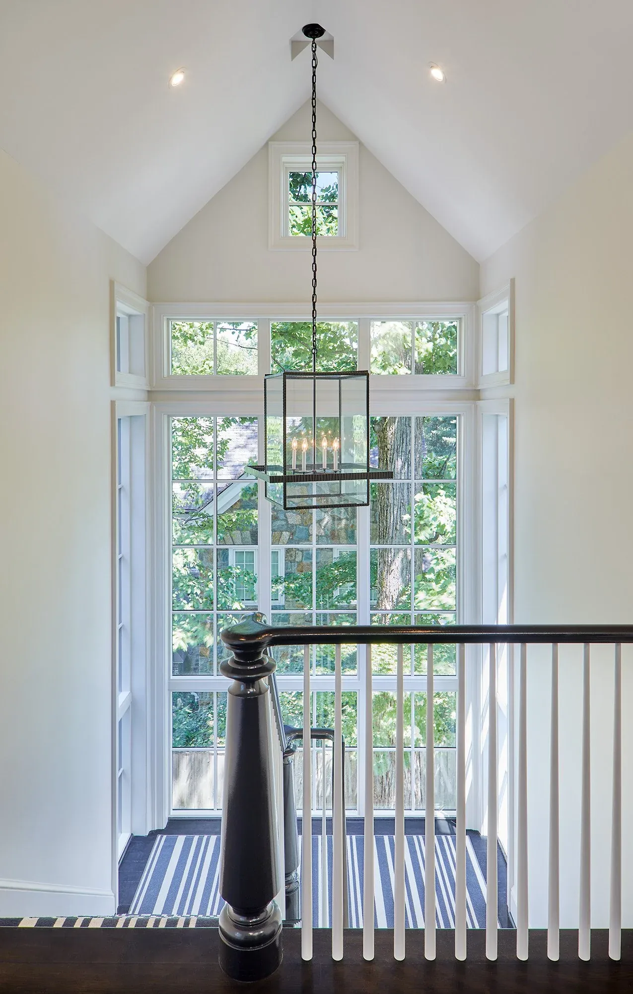 Stair landing featuring a tall bank of multi-pane windows and a modern rectangular chandelier by Moore Architects.