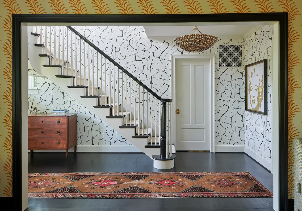 Interior hallway with a staircase featuring black handrail, abstract wall pattern, and a chandelier above.