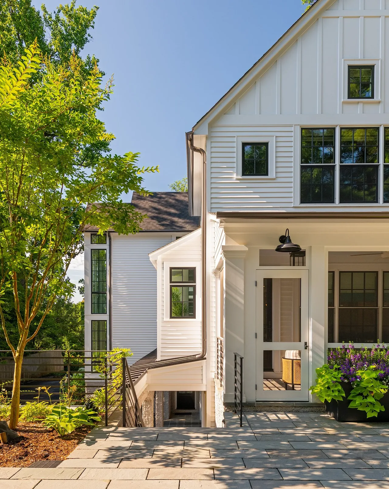 Side exterior of Cathedral View project showing white siding, black multi-pane windows, and a planted patio area.