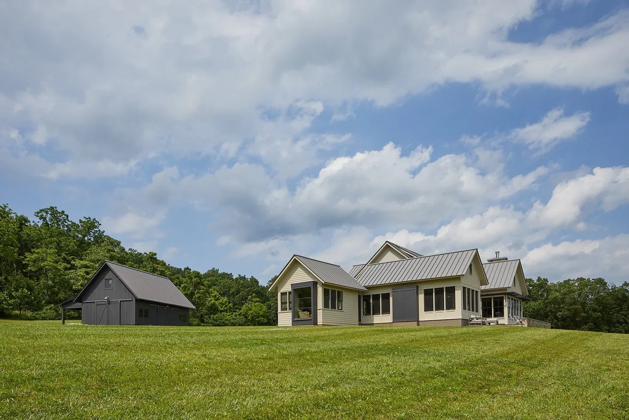 The Crimson Lane Residence features metal roofs and siding, located on a large open lawn with a detached outbuilding.