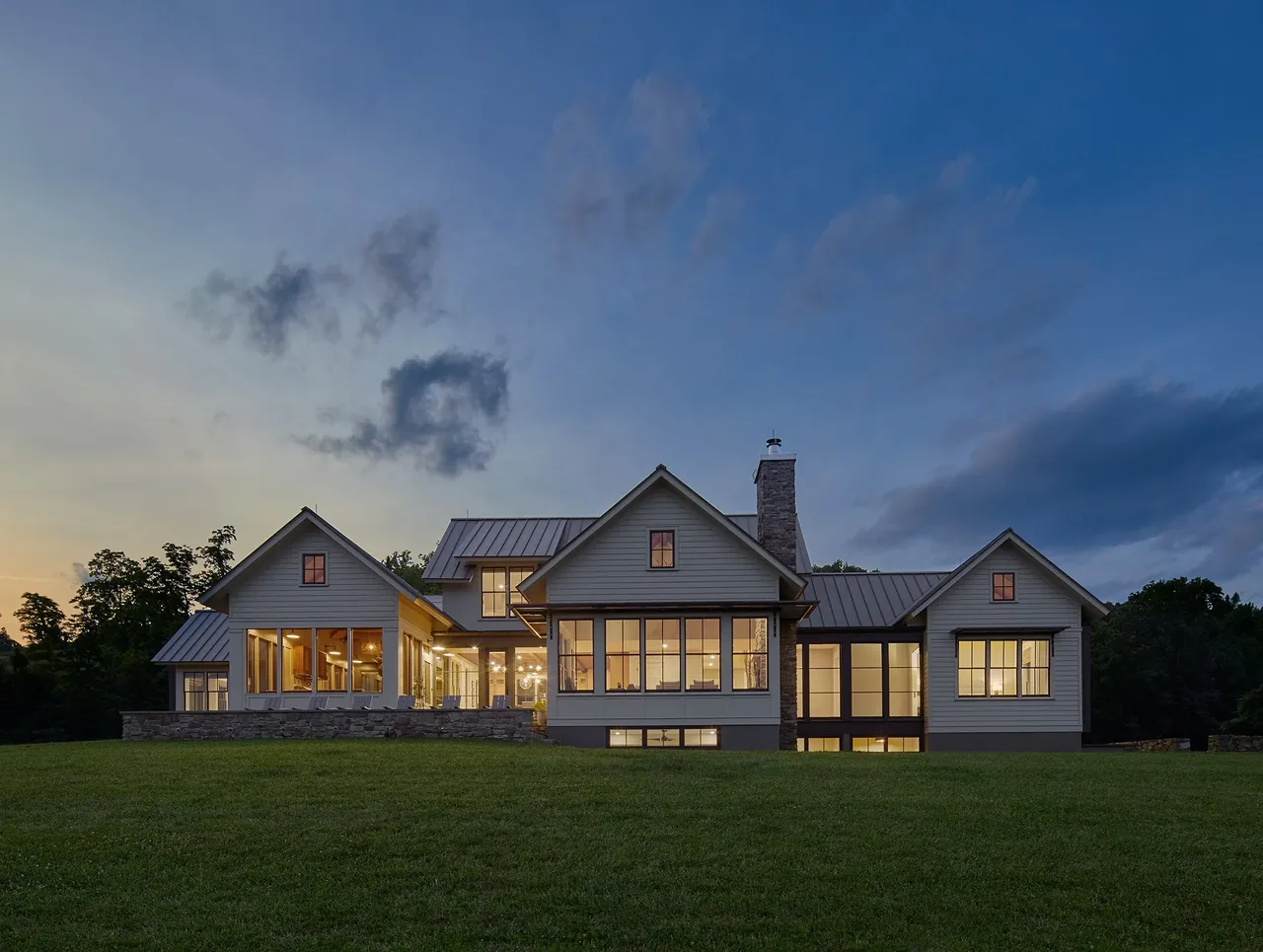 Crimson Lane Residence features multiple gable roofs and extensive window glazing at dusk, set against a large lawn.