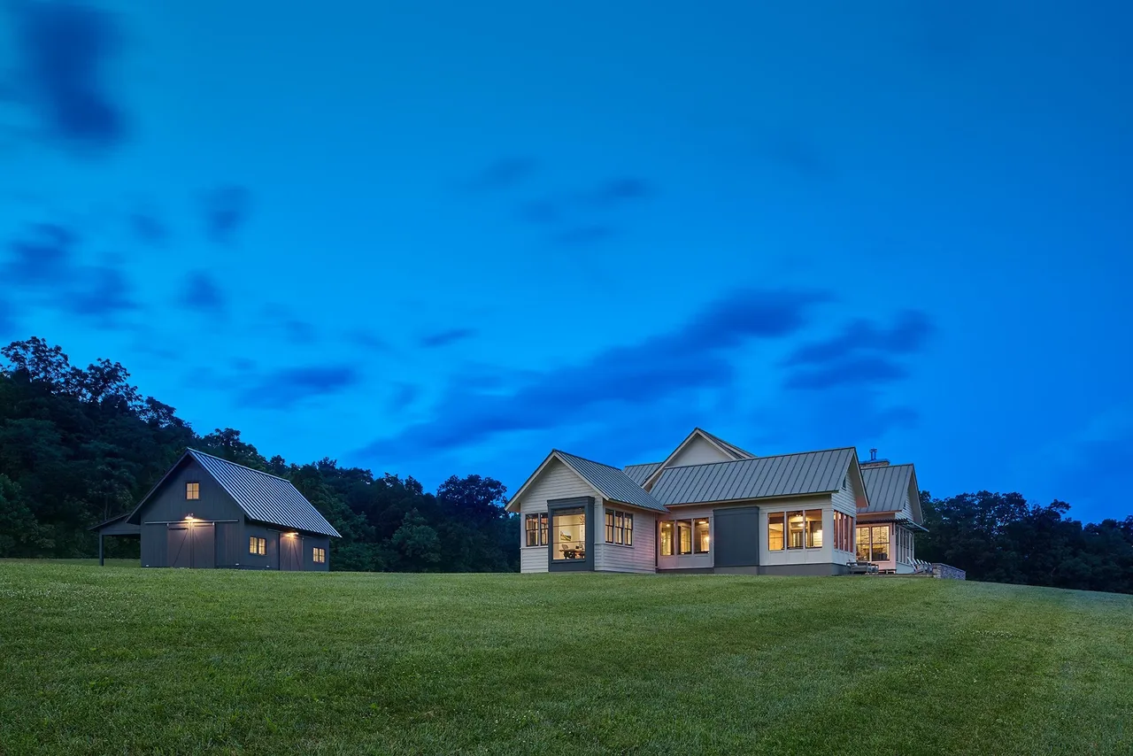 Crimson Lane Residence with metal roofs and illuminated windows at dusk, surrounded by large lawn and trees.