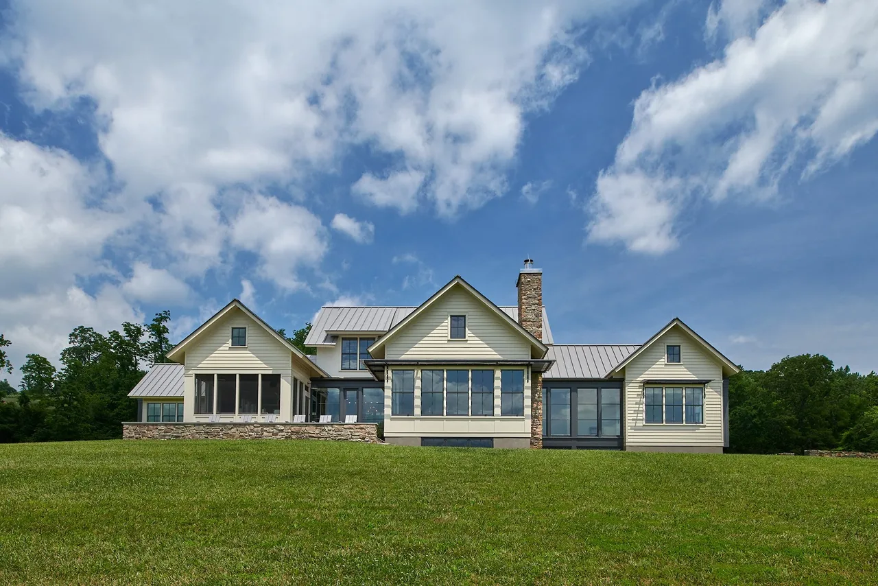 The Crimson Lane Residence showcases a farmhouse style with a stone chimney and metal roof over a large lawn.