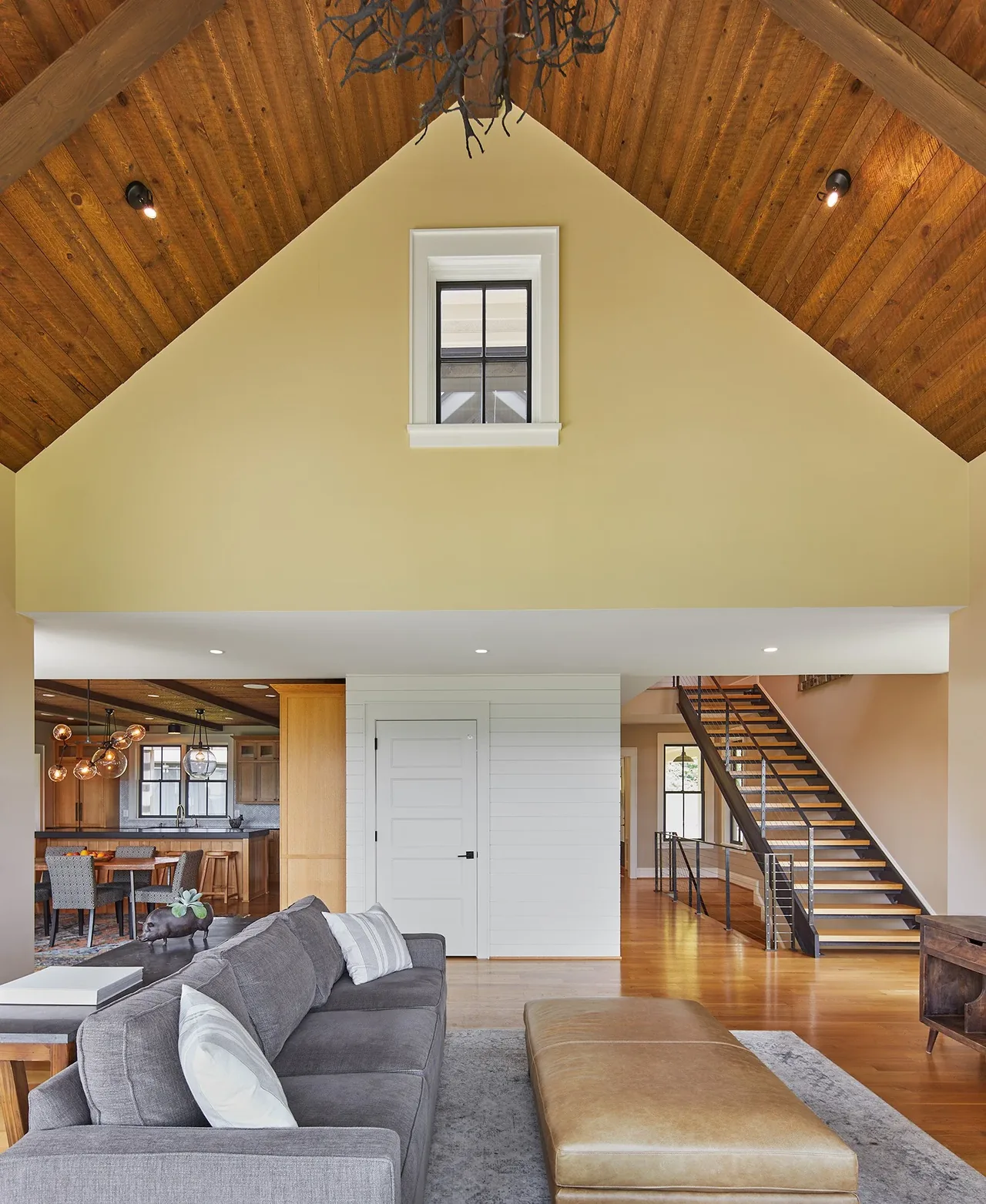 Living room with vaulted wood ceiling, gray sofa, and cable railing floating stairs leading upstairs.