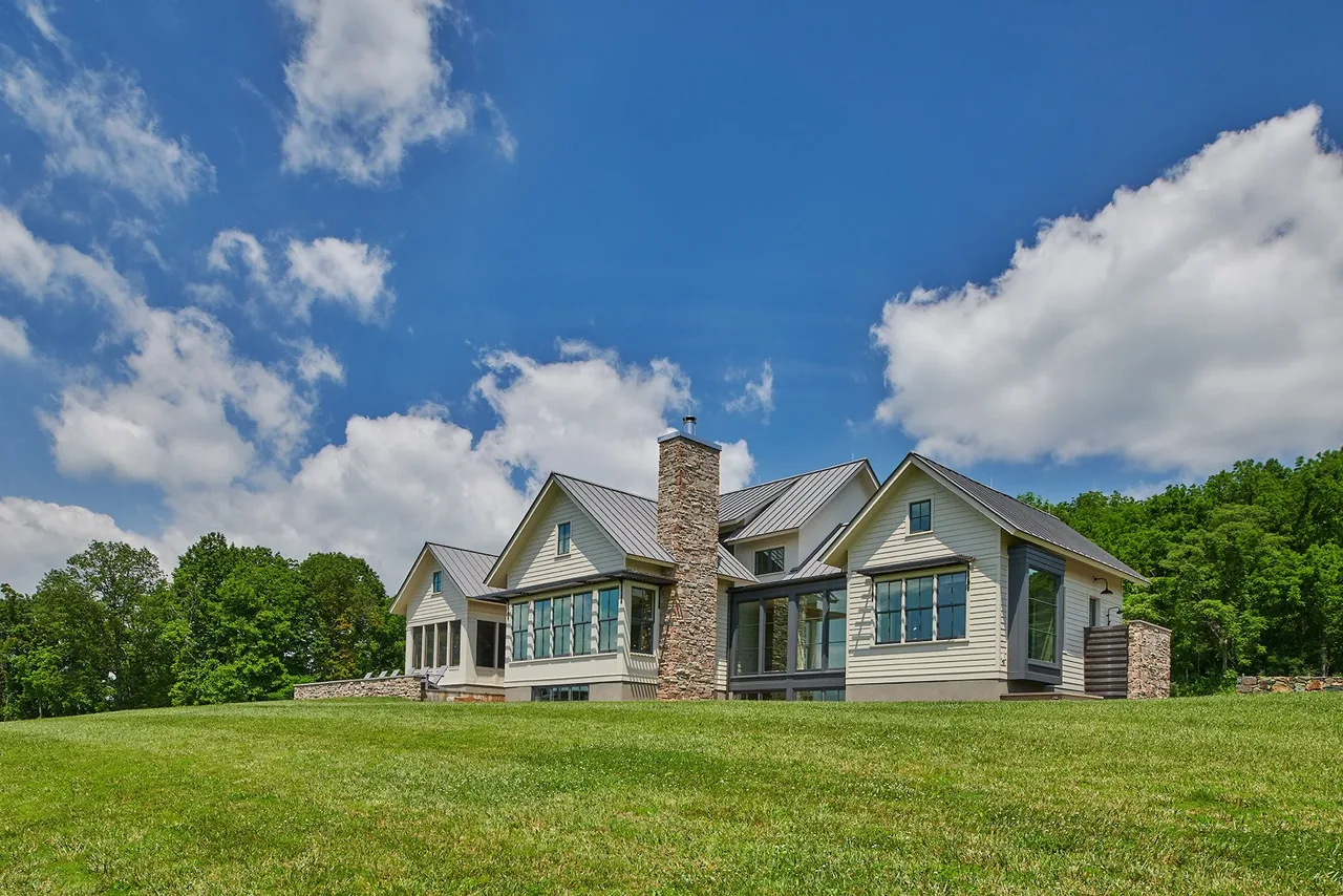 Crimson Lane Residence features a stone chimney, metal roof, and large lawn with gray window frames.