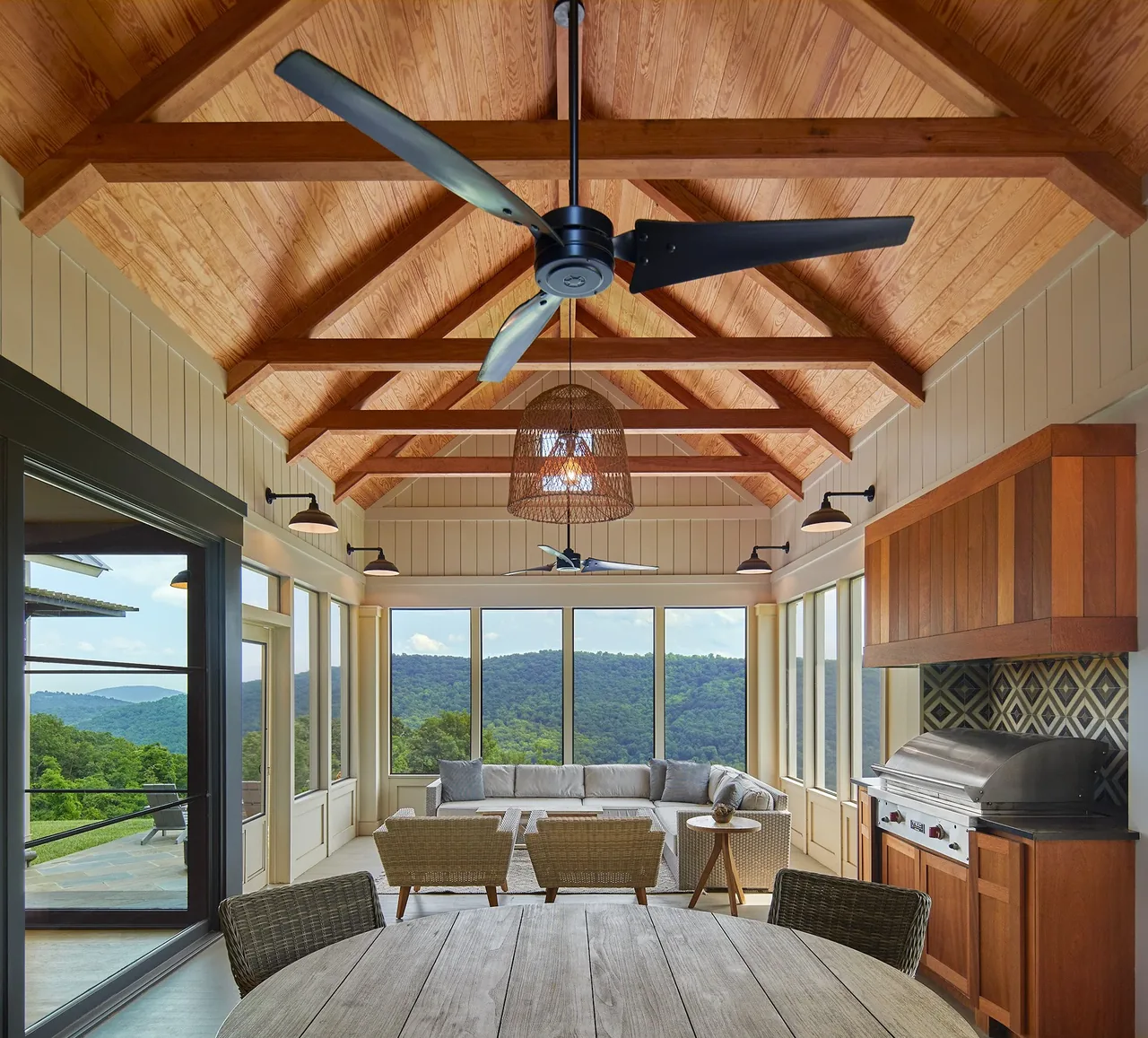 Covered patio with vaulted wood-beam ceiling, seating area, and built-in grill overlooking mountains.