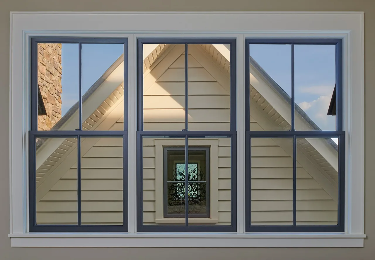 Gray-framed divided-lite windows overlook a beige clapboard siding gable with stone chimney visible on one side.