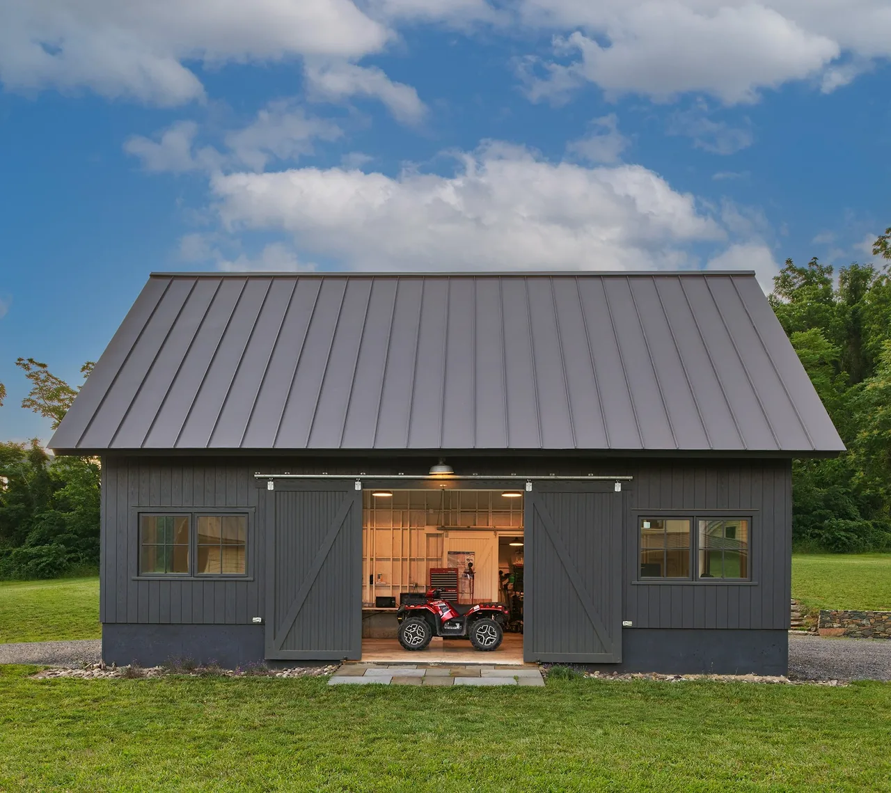 Crimson Lane Residence outbuilding features a metal gable roof, sliding barn doors, and a stone pathway leading to the entrance.
