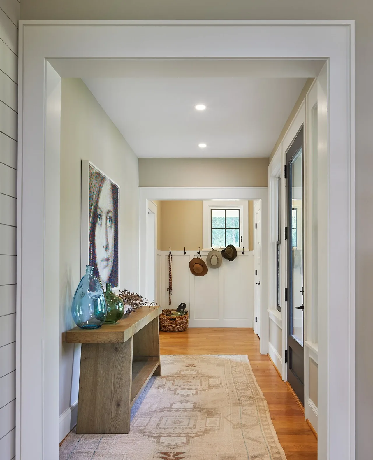 Hallway with wooden console, decorative vases, and wall hooks with hats in the Crimson Lane Residence.