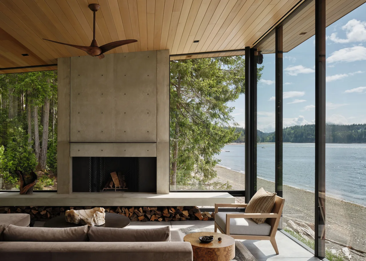 Living space with concrete fireplace and expansive lakefront views through floor-to-ceiling glass walls.